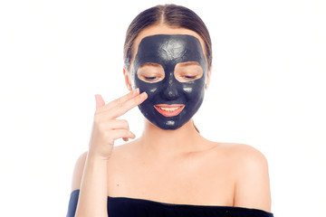 Brunette in a black mask for the face. Beautiful photo of a girl with perfect skin. A young girl cares for herself