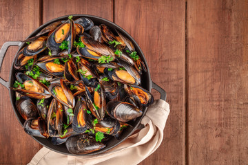 Marinara mussels, moules mariniere, in a cooking pot, overhead view, shot from the top on a dark rustic wooden background with a place for text
