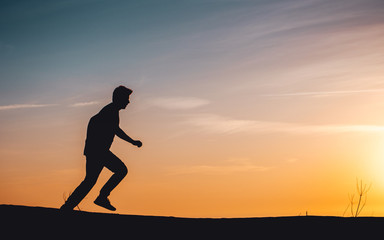 Side view of a active sport athlete man jumping and having fun in wide endless sand dunes at colorful, amazing sunset evening light. Lokken, Lønstrup in North Jutland in Denmark, Skagerrak, North Sea