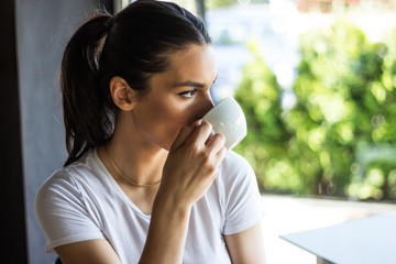 Obraz premium Portrait of young woman drinking coffee at table with notebook in cafe, Beautiful cute girl in the cafe near the window with coffee smiling