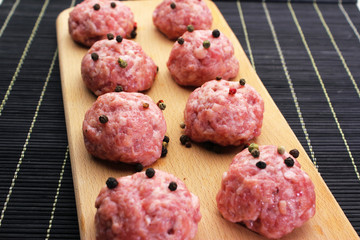 close up raw meatballs on a cutting board on a background of a black bamboo mat 