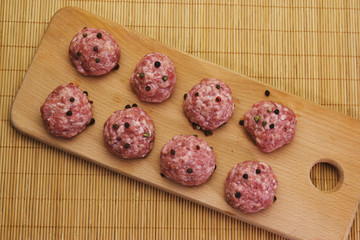 raw meatballs with peper beans  on a cutting board on a background of bamboo mat