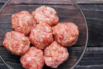 flat lay raw meat balls in a glass bowl on black wooden table top close up