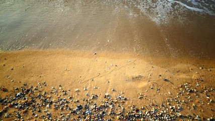 Sandy beach by the sea. Surf waves at the ocean. People walk along the beach.