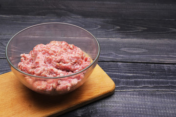raw minced meat in glass bowl on cutting board on black wooden table top surface