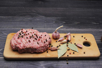 Burger. raw minced meat on cutting board with farlic and cpices onblack table top