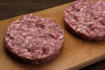 Burger.  Ground meat. Close up fresh raw minced beef steak burgers served on cutting board on empty dark wooden table top 