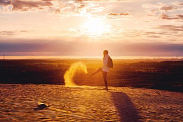 A girl walking in the endless sand dune beach landscape with sand in the air and shadow at colorful sunset light. Rubjerg Knude Lighthouse, L&oslash;nstrup in North Jutland in Denmark, Skagerrak, North Sea