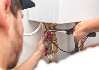The man is installing the heater system in the house and checking pipes by the wrench