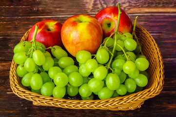 Three apples and grapes in a basket on a wooden table