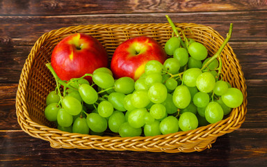 Two apples and grapes in a basket on a wooden table
