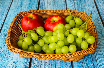 Two apples and grapes in a basket on a blue wooden table