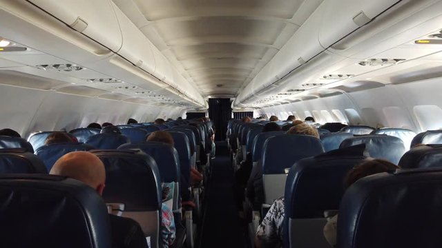 Economy class interior, aircraft cabin. Passengers sit in their seats.