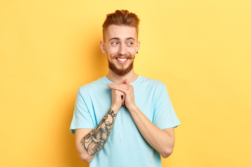 attractive funny cunning fair-haired male with satisfied expression holds hand above chin, looks thoughtfully and happily aside, stands over yellow wall.close up photo. barber
