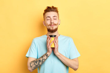 Handsome young man with closed eyes enjoying drinking a cup of coffee in his hands,isolated on a yellow background.coffee break, freetime, spare time, pleasure