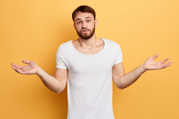 Unsure doubtful puzzled bearded man wearing white T-shirt shrugging his shoulders in questioning...