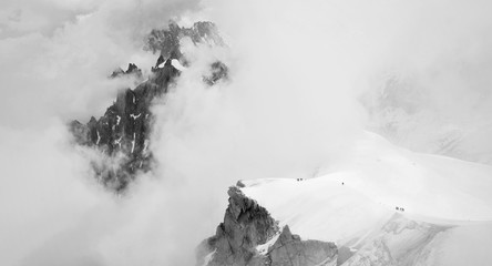 Dramatic panoramatic view of climbers in French Alps climbing among low clouds