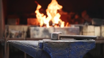 Hammer on anvil in forge on furnace with fire blur background in slow motion. Smithy workshop and workplace for manufacture of metal structures and for forging hot metal.