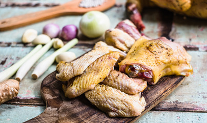 Pieces of fresh raw chicken parts on a cutting board on wooden old plank or table with blur Thai herbs and whole chicken. Chicken with Thai herbs prepared for cooking soup.