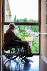 Back light silhouette of old man in wheelchair looking at window.