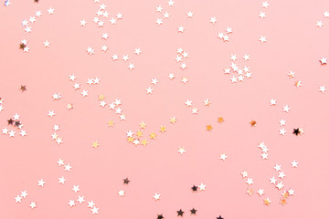 Holiday festive glitter background with pattern from scattered golden silver stars on light pink...