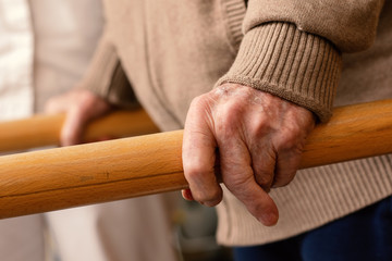 Detail of aged human hands grabbing parallel rehabilitation bars.
