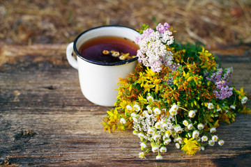 Herbal tea in an iron cup white yarrow flowers and St. John's Wort flowers on old wooden surface,...