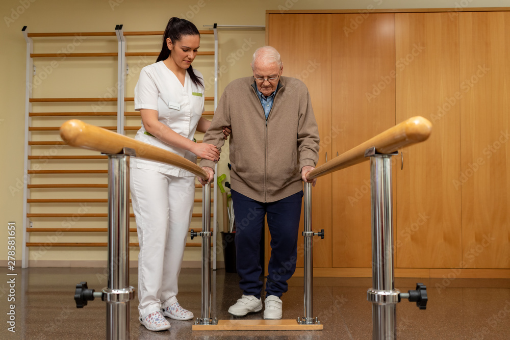 Wall mural Senior stroke patient doing rehabilitation in clinic with parallel bars.