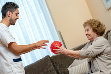 Senior woman and physiotherapist doing coordination exercise with plastic ball