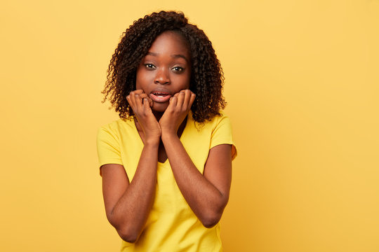 scared emotional american woman keeps , hands on cheeks, being shocked to listen to new, stares at camera, isolated over yellow background. girl in casual stylish clothes expresses great surprisment