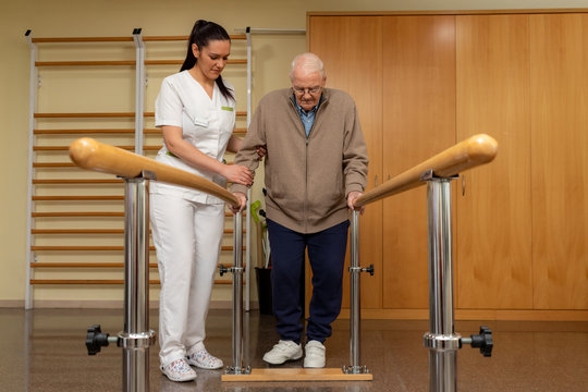 Senior stroke patient doing rehabilitation in clinic with parallel bars.