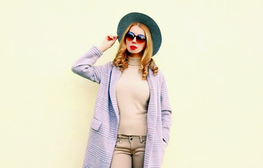 Stylish woman posing in pink coat, round hat on wall background