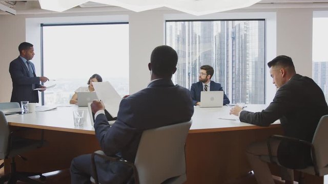 Mature Businessman Standing Giving Presentation To Colleagues Sitting Around Table In Modern Office 