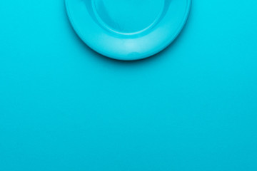Minimalist photo of round ceramic plate over turquoise blue background with copy space. Top view of blank dish on blue table central composition. Half of plate is in the shot