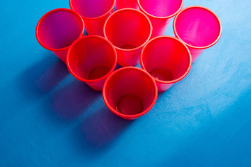 Colored plastic cups are a triangle on a blue background. Composition of disposable glasses for drinks. Plastic utensils.