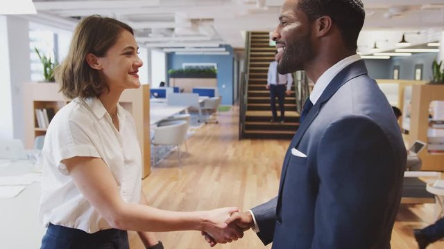 Two Businesswoman And Businessman Meet And Shake Hands In Modern Open Plan Office