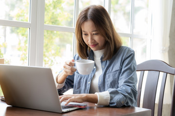 Happy Asian woman shopping online and paying by credit card in coffee shop. technology and ecommerce concept