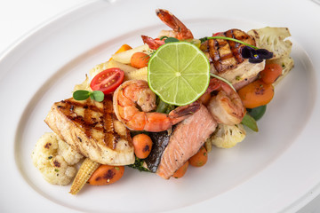 Luxurious seafood salad with shrimp, octopus, squid, fish, lime, cherry tomatoes, grilled vegetables and greens Banquet festive dishes. Fine dining restaurant menu. White background.