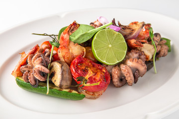 Luxurious seafood salad with shrimp, octopus, squid, fish, lime, cherry tomatoes, grilled vegetables and greens Banquet festive dishes. Fine dining restaurant menu. White background.