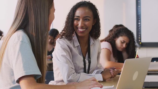 Woman Teacher Giving One To One Support To Female Student Working At Desk On Laptop