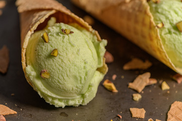 Balls of pistachio ice cream in waffle cones on a dark background.