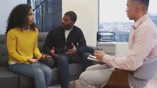 Unhappy Couple Sitting On Couch Meeting With Male Counsellor In Office