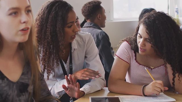 Woman Teacher Giving One To One Support To Female Student Working At Desk On Digital Tablet