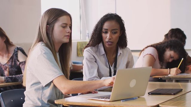 Woman Teacher Giving One To One Support To Female Student Working At Desk On Laptop
