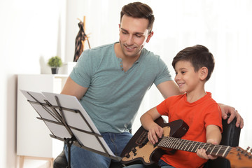 Little boy playing guitar with his teacher at music lesson. Learning notes