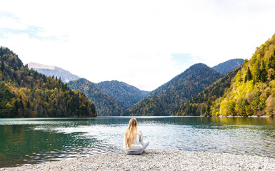 Fototapeta na wymiar Girl in a gray tracksuit on the background of lake Ritsa in Abkhazia in autumn