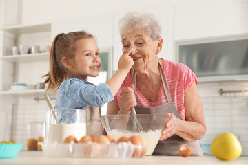 Cute girl and her grandmother cooking in kitchen