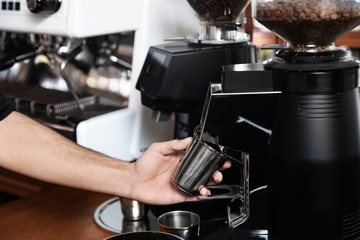 Barista with metal cup using coffee grinding machine in cafe, closeup