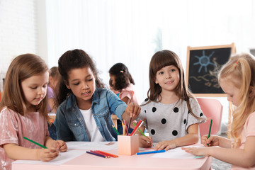 Adorable children drawing together at table indoors. Kindergarten playtime activities