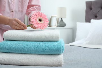 Woman putting flower on stack of clean towels in bedroom. Space for text